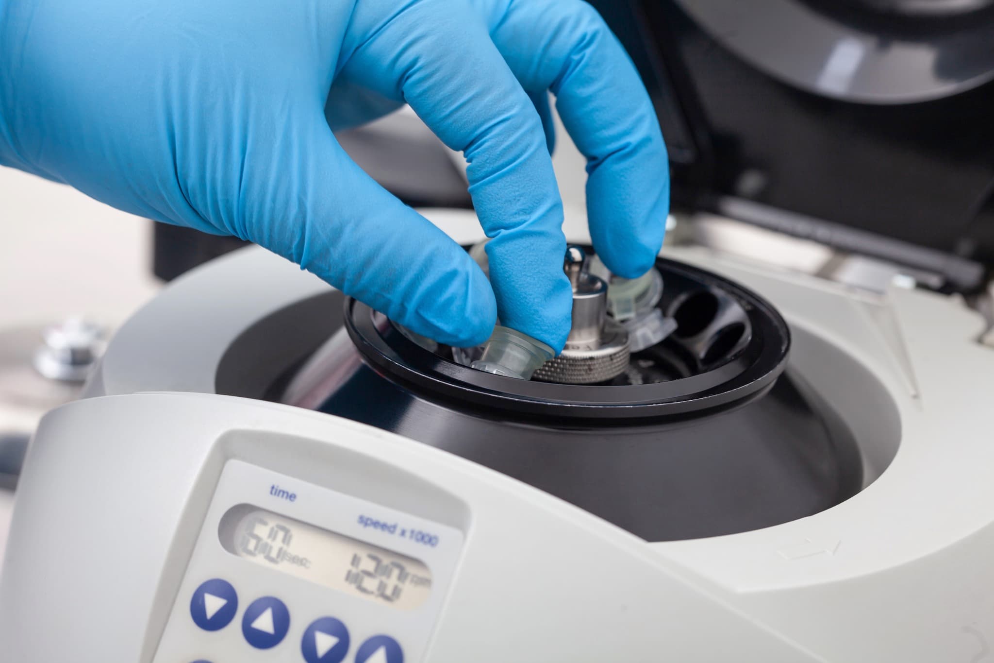 Gloved hand handling a centrifuge in a clinical lab